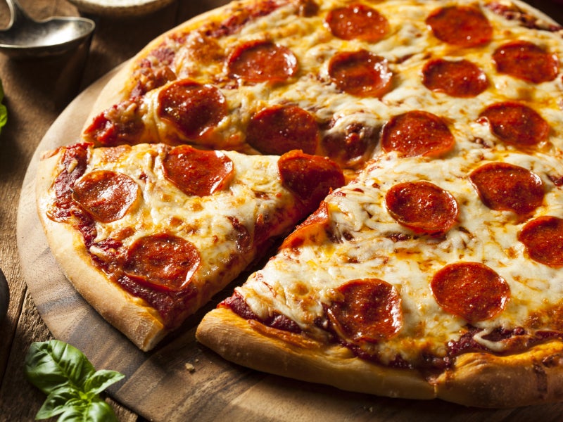 Close-up of a pepperoni pizza with a slice being pulled away, served on a wooden board.